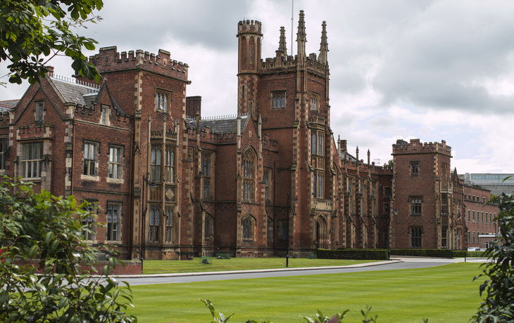Historisches Backsteingebäude mit gepflegtem Rasen und bewölktem Himmel.