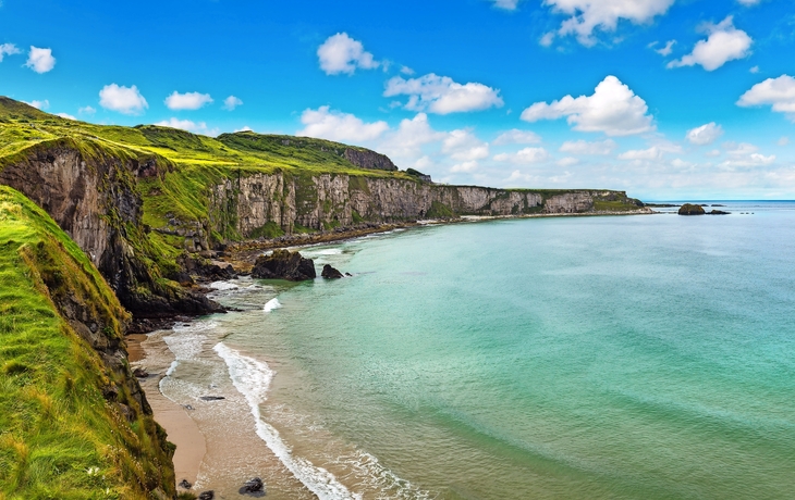 Küstenblick mit grünen Klippen und blauem Himmel.