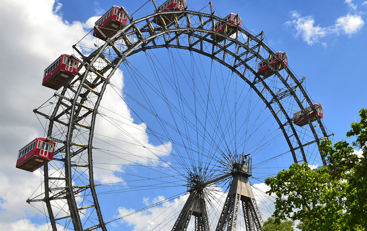 Riesenrad mit roten Gondeln vor einem blauen Himmel mit weißen Wolken.