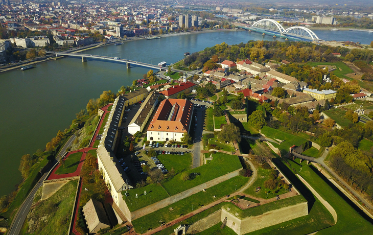 Luftaufnahme einer Festung am Fluss mit Stadt und Brücke im Hintergrund.