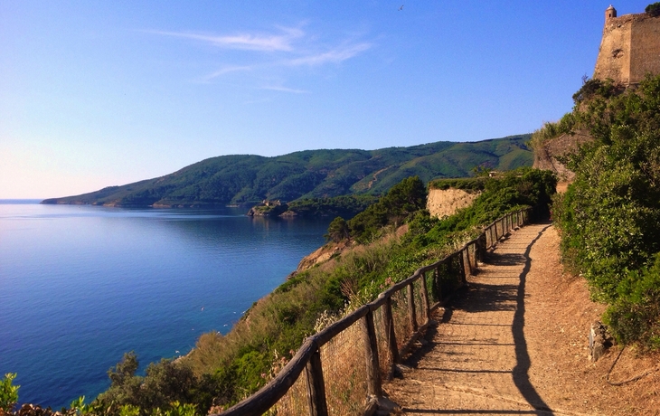 Küstenpfad mit Blick auf das Meer und Hügel im Hintergrund.