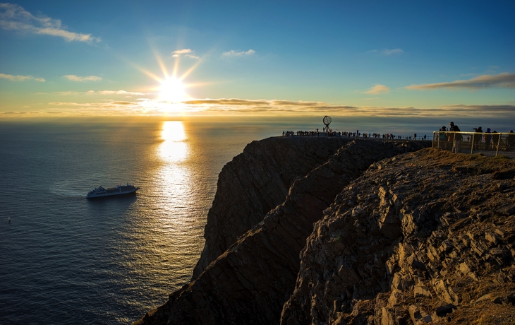 Klippe bei Sonnenuntergang am Meer mit Schiff und Nordkap-Monument.
