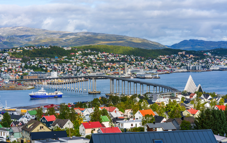 Küstenstadt mit Brücke, Schiff und Bergen im Hintergrund.