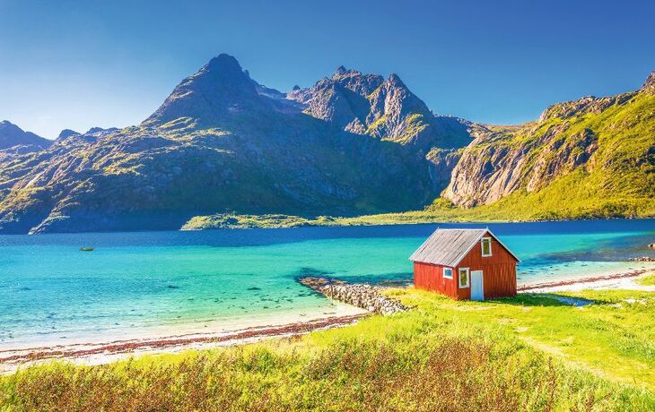 Rotes Holzhaus am türkisblauen See mit Bergen im Hintergrund.