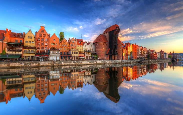 Bunte Gebäude spiegeln sich im Wasser eines Flusses bei Sonnenuntergang.