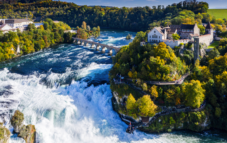 Luftaufnahme der Rheinfall-Wasserfälle mit umliegendem Grün und Gebäuden im Hintergrund.