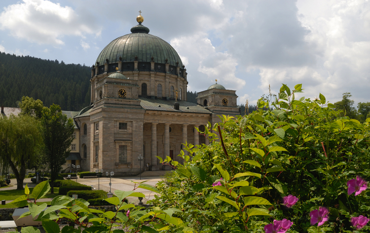 Große Kuppelkirche mit Blumen im Vordergrund, bewölkter Himmel.