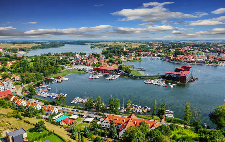 Stadtansicht mit Hafen, grüner Landschaft und Wasser an einem sonnigen Tag.