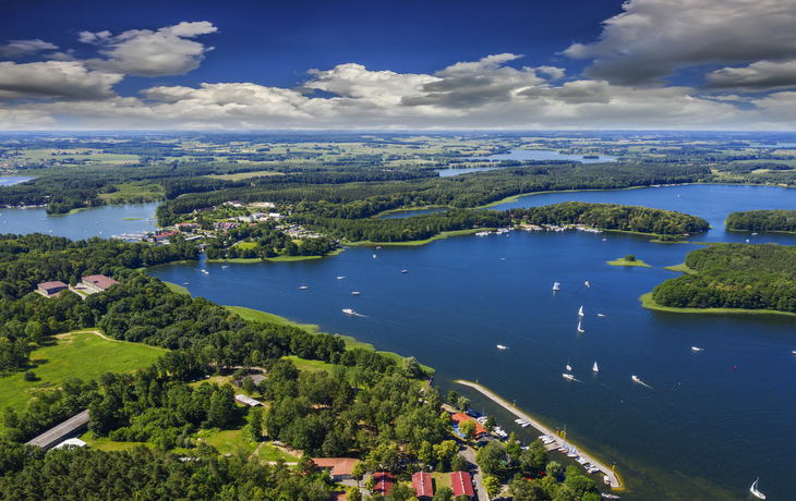 Luftaufnahme eines Sees mit Segelbooten und umgebendem Waldgebiet.
