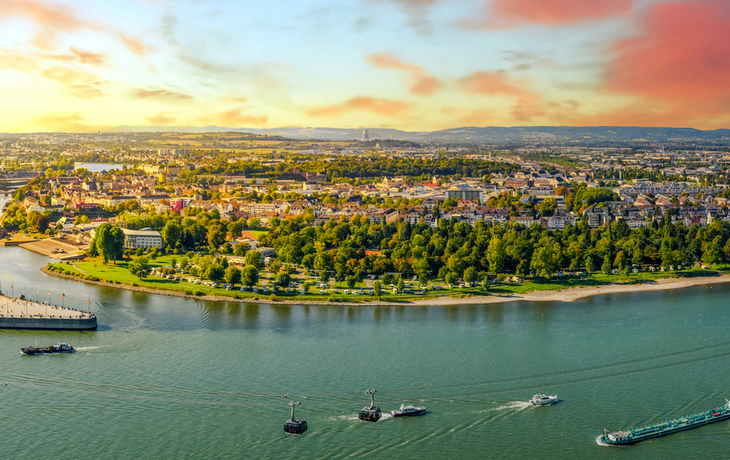 Panoramablick auf eine Flusslandschaft bei Sonnenuntergang mit Stadt und Schiffen.