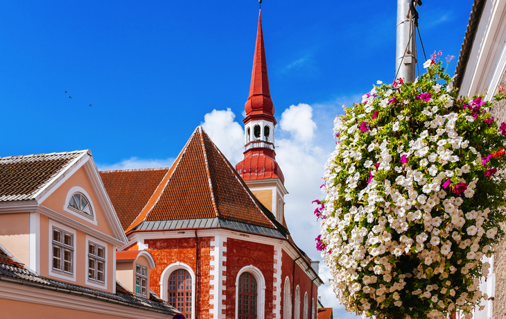 Kirchturm und Blumenampel vor blauem Himmel in einer Altstadt.