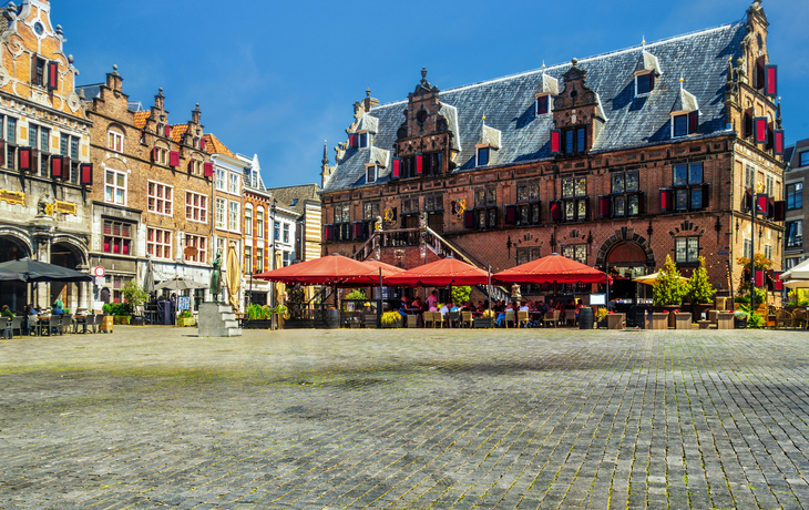 Historischer Platz mit alten Gebäuden und Straßencafés bei sonnigem Wetter.