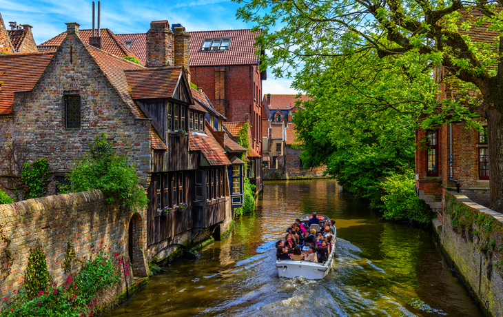Boot mit Touristen auf Kanal zwischen alten Gebäuden und Bäumen