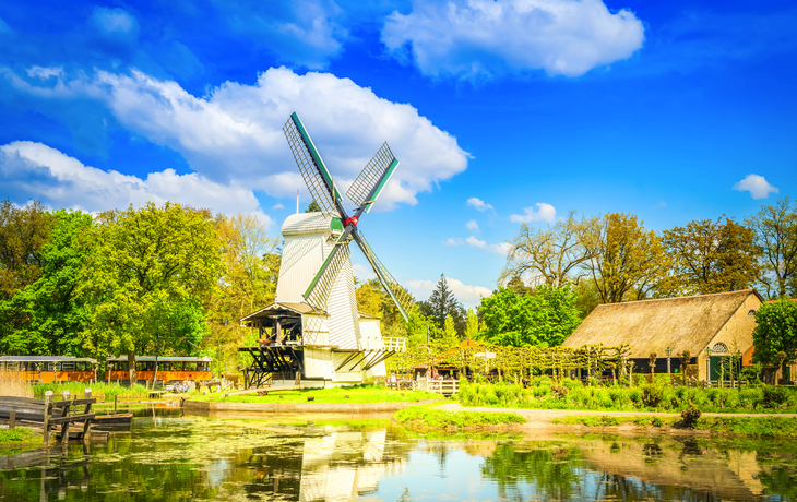 Windmühle und Haus am Teich unter blauem Himmel mit Wolken