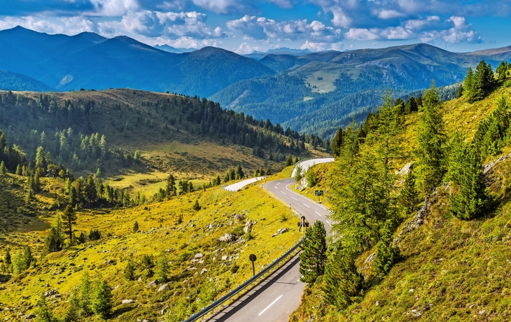Bergstraße mit grüner Landschaft und bewaldeten Hügeln unter blauem Himmel