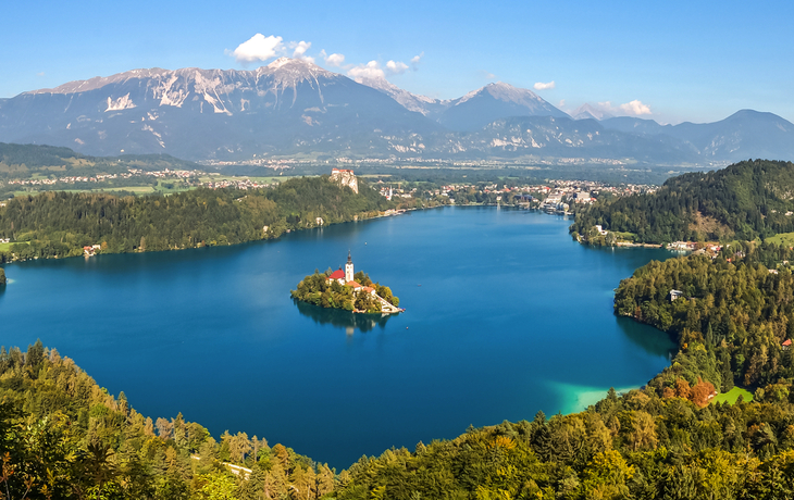 Blick auf den Bleder See mit Insel und Kirche, umgeben von Bergen und Wald.