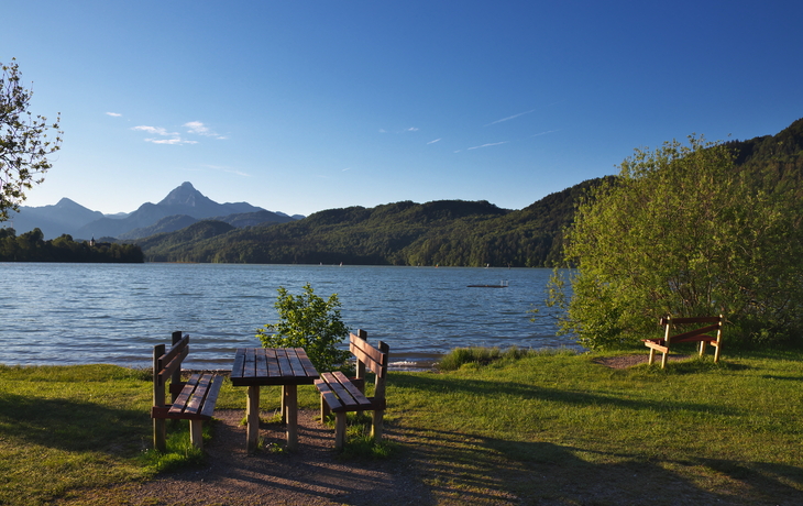 Holzbänke und -tische mit Blick auf einen See und Berglandschaft im Hintergrund