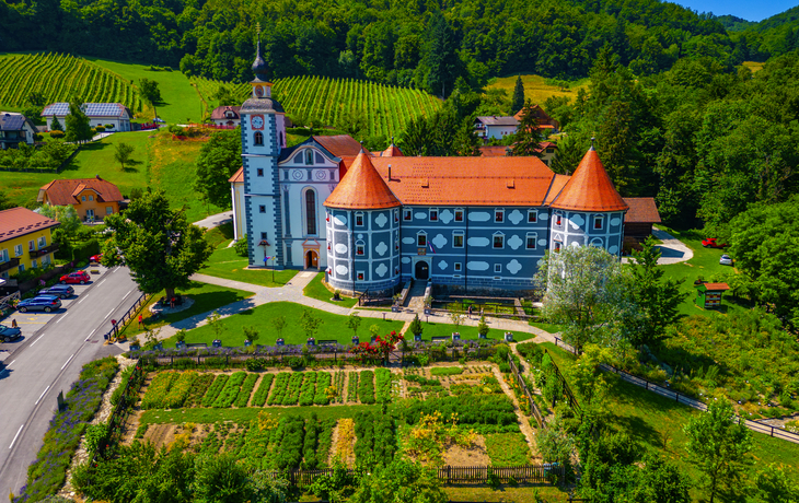 Historisches Schloss mit Garten, umgeben von grünen Hügeln.