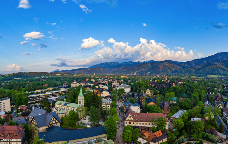 Panorama einer Stadt mit Kirche und Bergen im Hintergrund bei klarem Himmel.