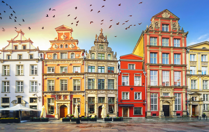 Historische Gebäude am zentralen Platz mit vorbeifliegenden Vögeln im Himmel.