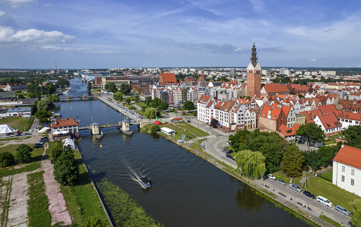 Stadtansicht mit Fluss und Kirche unter blauem Himmel.