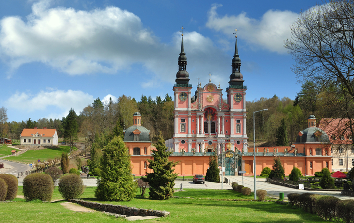 Barockkirche in einer grünen Parklandschaft unter blauem Himmel mit Wolken.