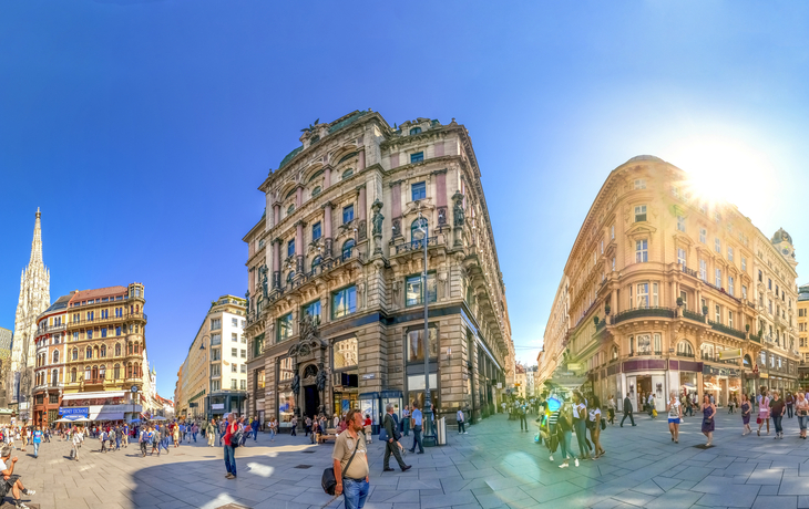 Panoramablick auf historischen Platz mit Gebäuden und Menschen bei Sonnenschein.