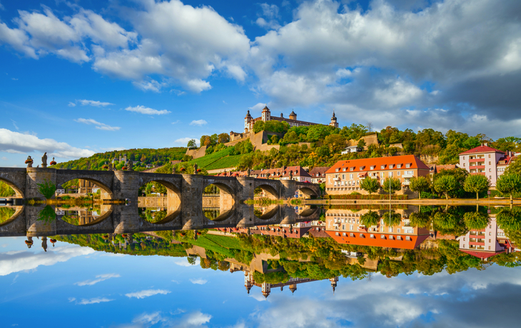 Brücke über Fluss mit Schloss und bewölktem Himmel im Hintergrund.