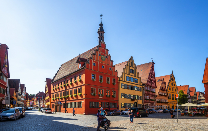 Bunte historische Gebäude in einer sonnigen Altstadt mit Menschen und Autos.