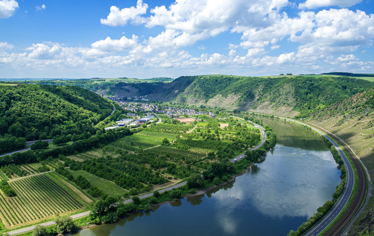 Fluss in hügeliger Landschaft mit Weinbergen und blauem Himmel.
