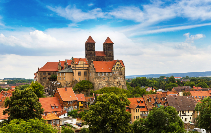Schloss und Altstadt von Quedlinburg, umgeben von Bäumen und wolkigem Himmel.