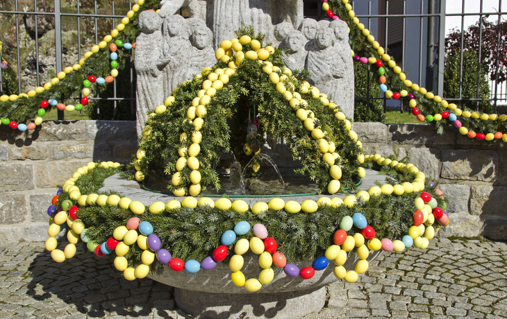 Osterbrunnen mit buntem Osterschmuck aus Eiern und Grünzweigen.