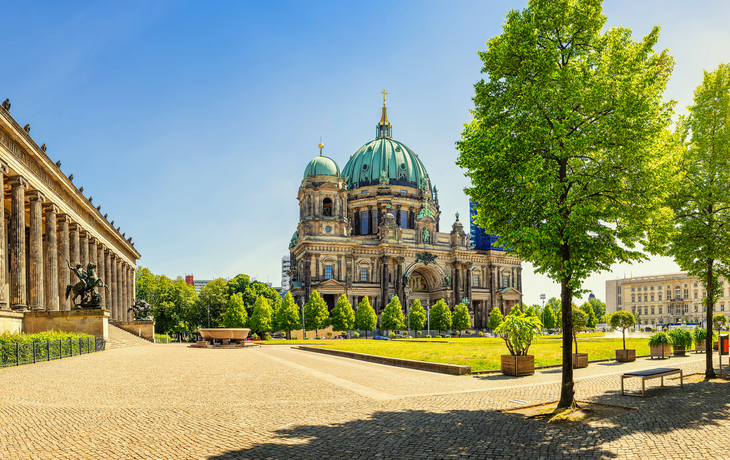 Berliner Dom bei sonnigem Wetter mit Bäumen und Architektur im Vordergrund.