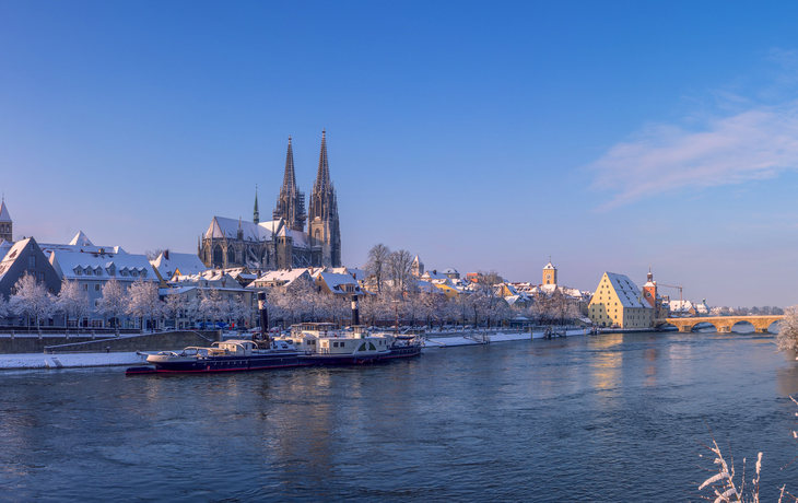 Verschneite Stadtlandschaft mit Fluss und gotischer Kathedrale.