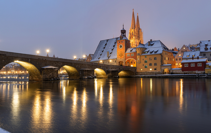 Steinbrücke und Altstadt im Winter mit beleuchtetem Kirchturm im Hintergrund
