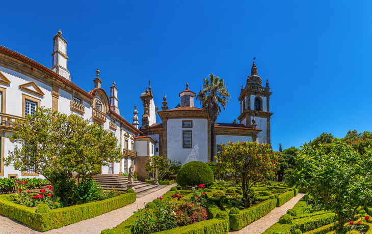 Historische Villa mit Türmen und gepflegtem Garten bei klarem Himmel.