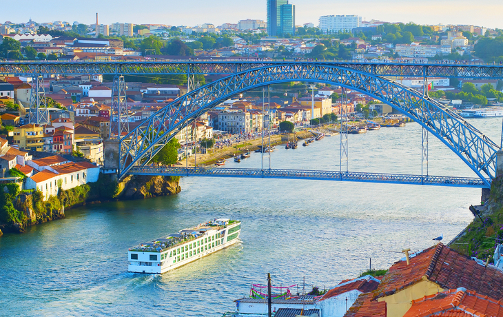 Blick auf Brücke über Fluss in Stadt mit Boot und Altbauten im Vordergrund.