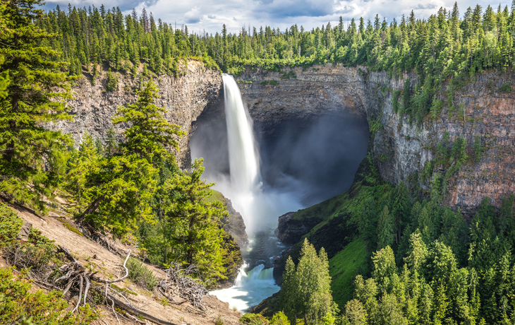 Wasserfall in bewaldeter Schlucht bei sonnigem Wetter.