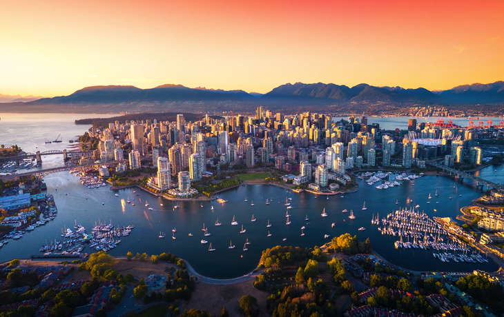 Luftaufnahme von Vancouver bei Sonnenuntergang mit Bergen im Hintergrund.