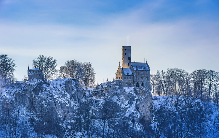 Schloss auf schneebedecktem Hügel im Winter bei blauem Himmel.