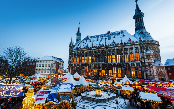 Weihnachtsmarkt mit festlich beleuchteten Ständen vor einem alten Gebäude im Winter.