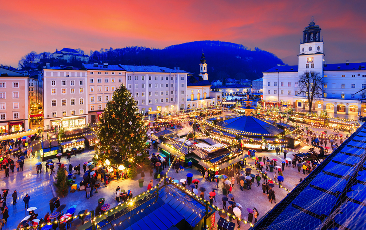 Weihnachtsmarkt in einer Stadt bei Sonnenuntergang mit beleuchtetem Tannenbaum