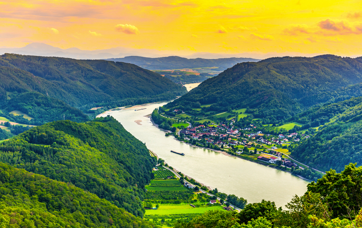Landschaft mit Fluss, Bergen und Dorf unter einem gelblichen Himmel.