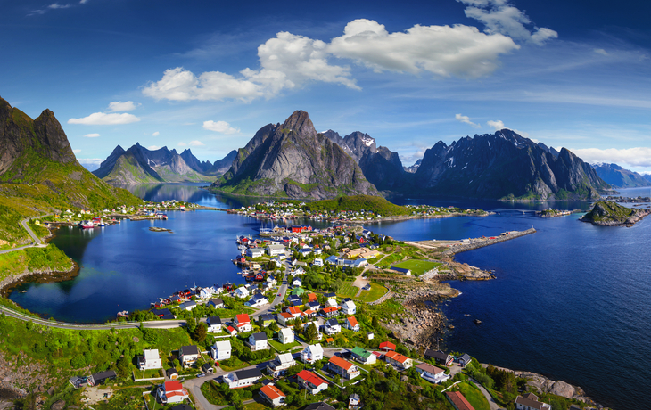 Küstenlandschaft mit Fjord, bunten Häusern und Bergen im Hintergrund.