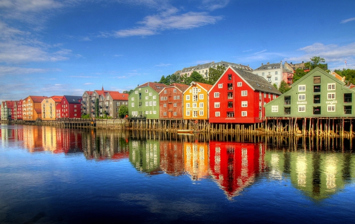 Bunte Holzhäuser spiegeln sich im Wasser unter blauem Himmel.