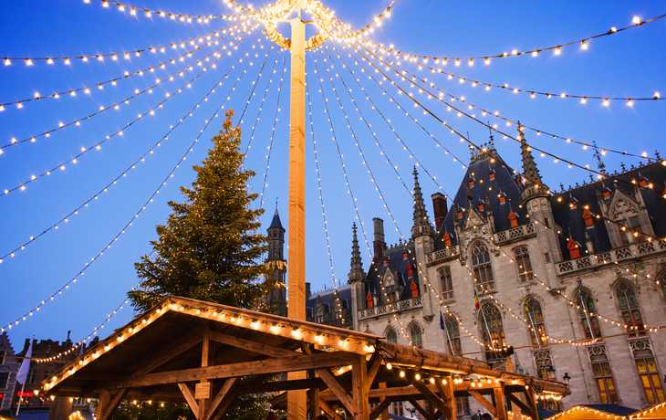 Weihnachtsmarkt bei Dämmerung, mit Lichtern und historischer Architektur im Hintergrund.