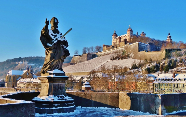 Statue auf einer Brücke vor einer verschneiten Festung und Stadt im Hintergrund.
