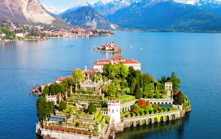 Insel mit Schloss und Garten in einem See vor Bergkulisse