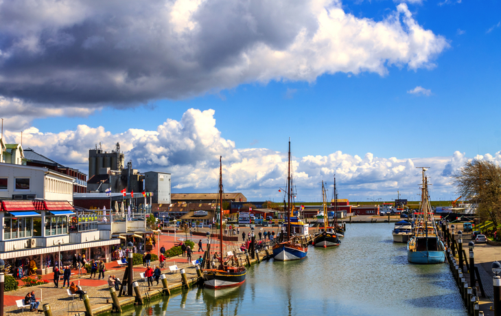 Hafen mit Booten, Gebäuden und Promenade unter wolkigem Himmel