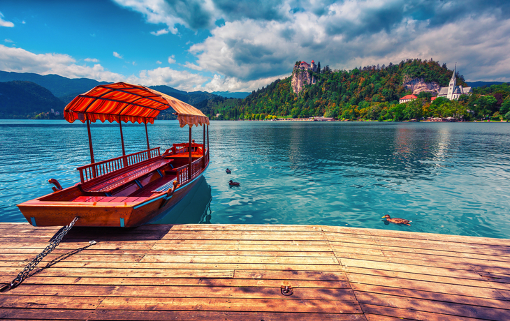 Holzboot am Steg mit Blick auf einen See und bewaldete Hügel im Hintergrund